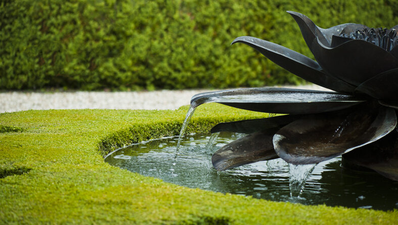 Sculptural bronze water feature in a circular pool set in a lawn