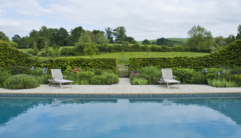 Swimming pool framed by clipped hedges looking out to open countryside