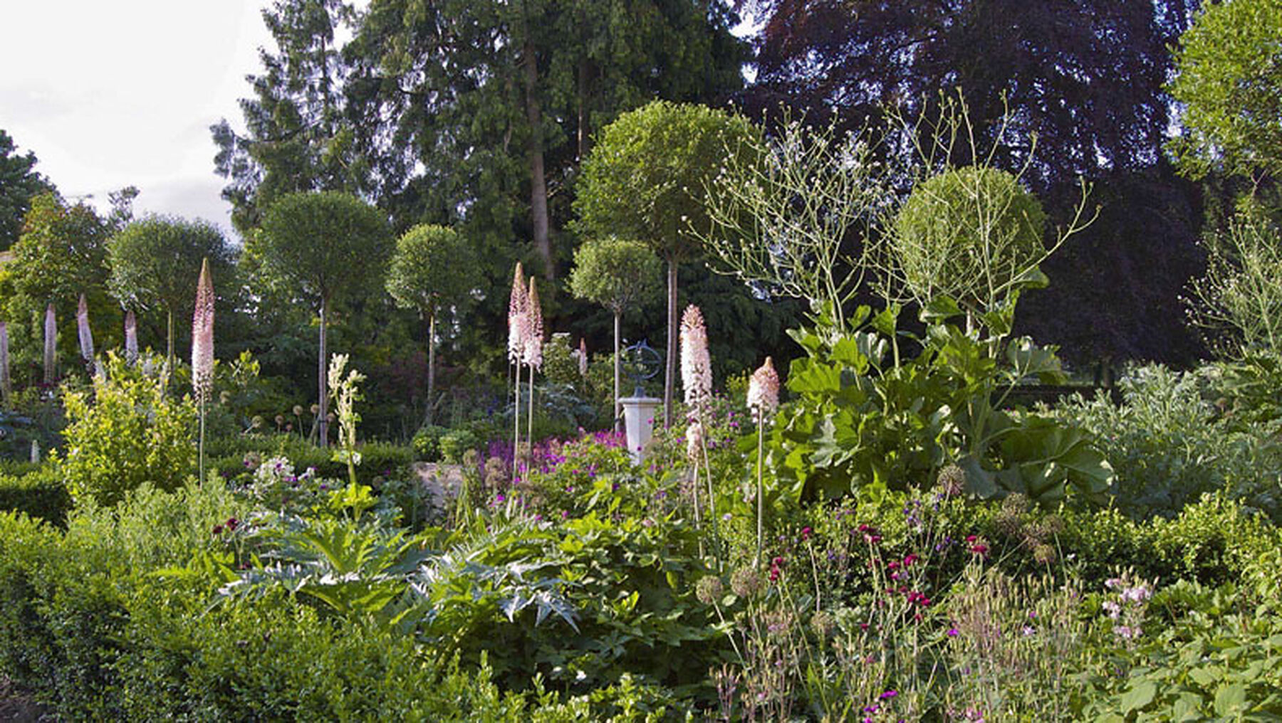 A mature herbaceous garden with standard trees, foxtail lilies and a sundial, designed by Justin Spink